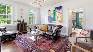 A living room with a leather sofa, a coffee table, a patterned rug, and a large abstract painting. - West End Stylish & Creative Home w/ Parking (Portland)