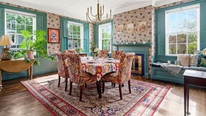 A dining room with a table set for six, surrounded by floral-patterned chairs, a chandelier, and a fireplace. - West End Stylish & Creative Home w/ Parking (Portland)