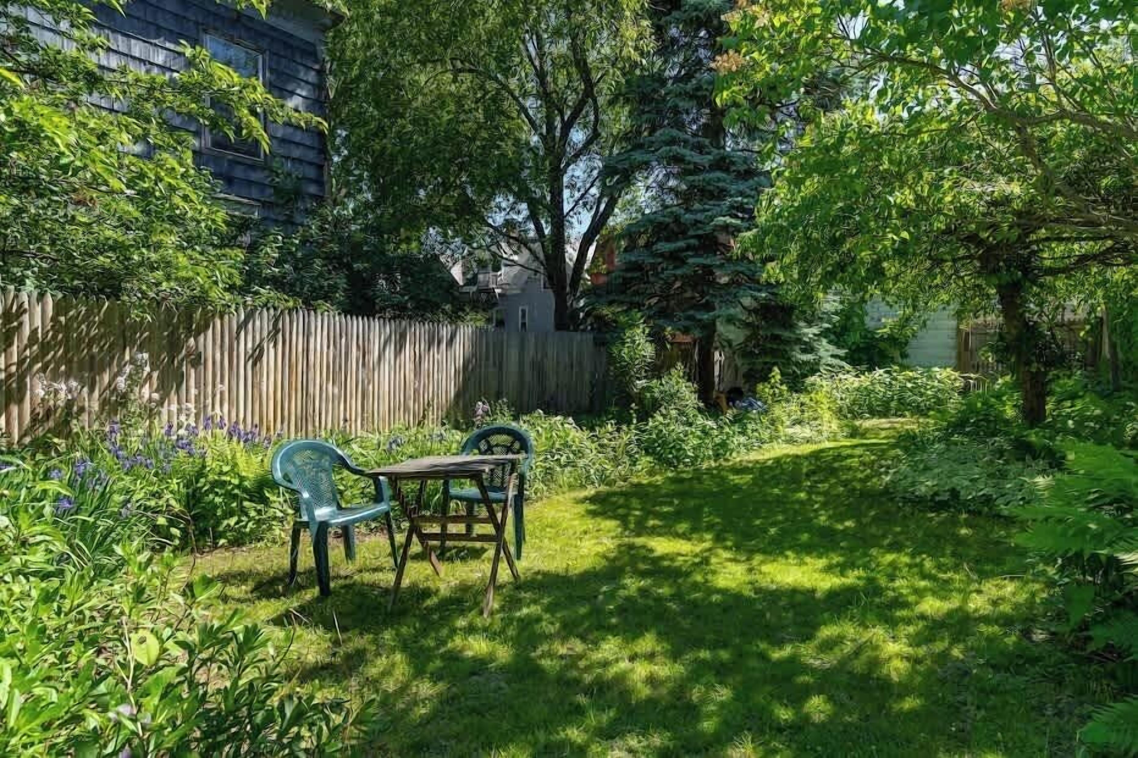 A backyard with a wooden fence, a table with chairs, and various plants.