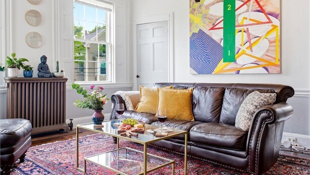 A living room with a leather sofa, a coffee table, a patterned rug, and a large abstract painting on the wall. - West End Stylish & Creative Home w/ Parking (Portland)