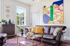A living room with a leather sofa, a coffee table, a patterned rug, and a large abstract painting on the wall. - West End Stylish & Creative Home w/ Parking (Portland)