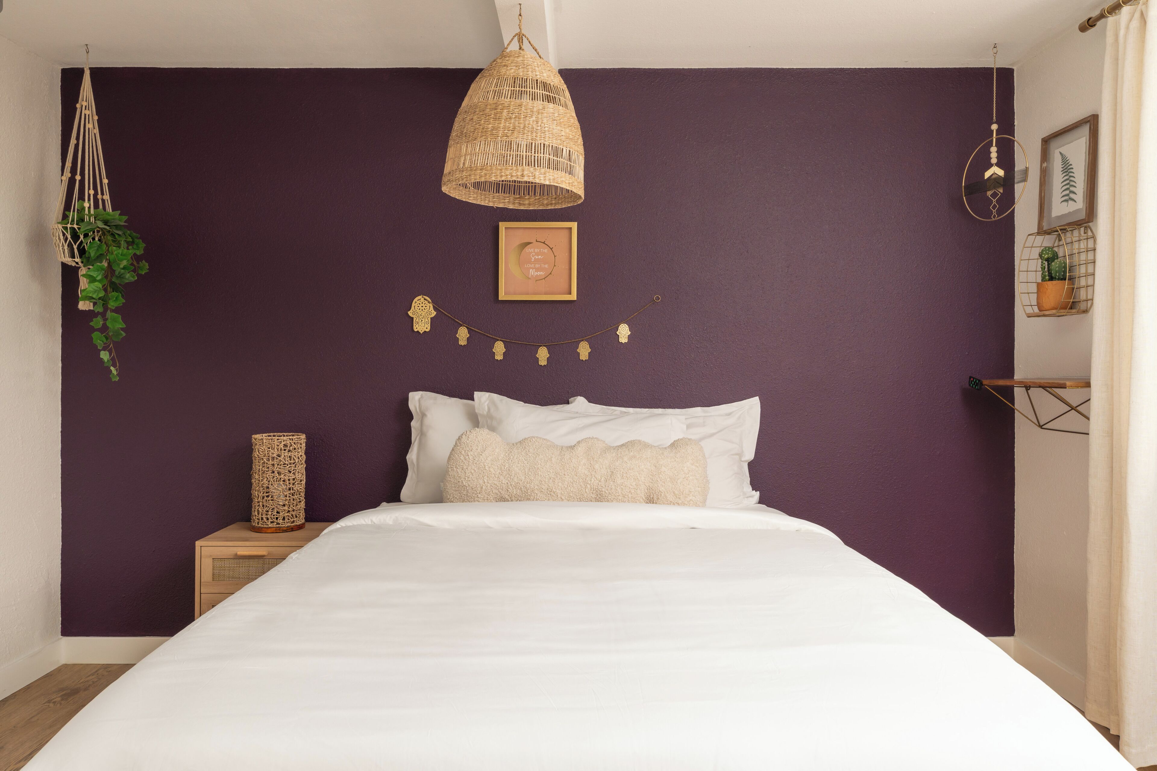 A bedroom with a bed, a hanging light fixture, a wall-mounted picture, and a small plant.