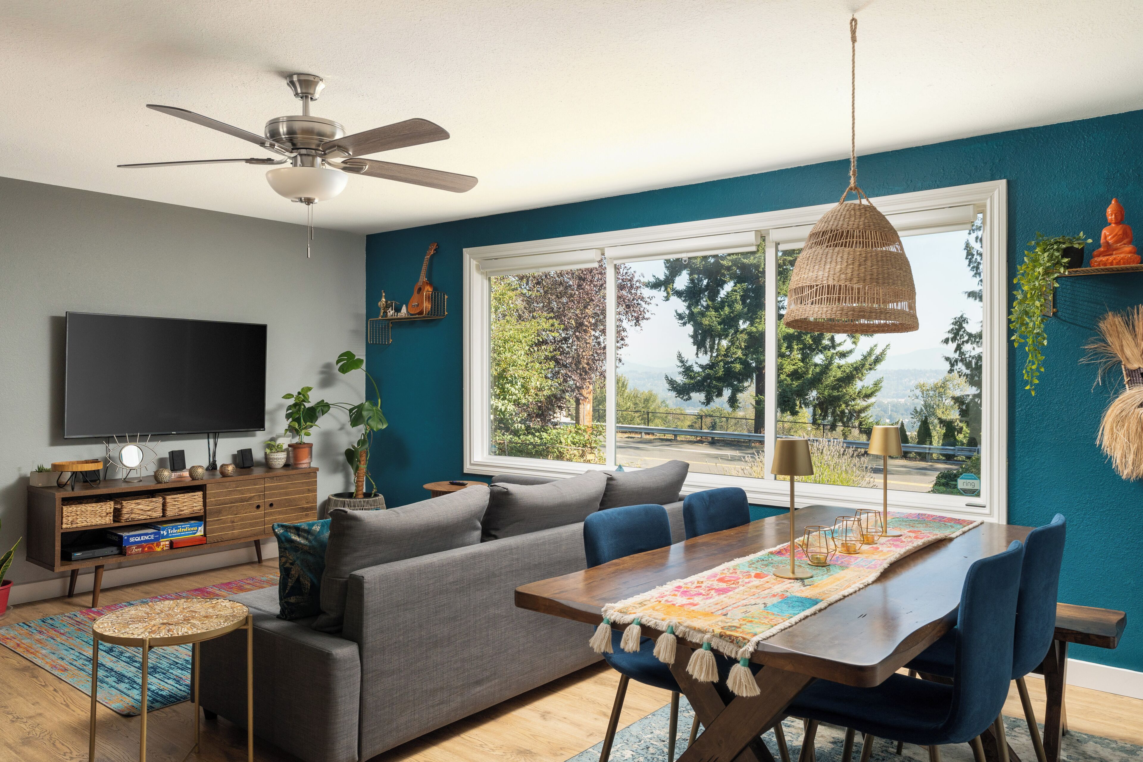 Een woonkamer met een bank, eettafel, stoelen, een televisie en een plafondventilator.