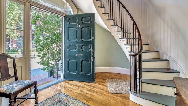 A grand entryway with a large black door, a wooden bench, a staircase with a metal railing, and a view of greenery outside. - Two Beautiful Apartments- Ideal for Groups! (Portland)
