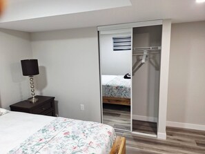 A bedroom with a bed, a nightstand, a lamp, a wardrobe, and a mirror. - Cozy Two Bedrooms Basement Suite (Winnipeg)