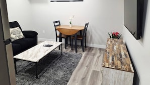Una sala moderna con una mesa de comedor, sillas negras, un sofá negro, una mesa de centro de mármol, un tapete gris y una mesita auxiliar de madera con flores rojas.