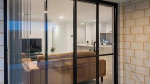 Een modern interieur met een bank, een televisie en een keukenruimte zichtbaar door een glazen deur.