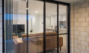 Un interior modern amb un sofà, una televisió i una zona de cuina visible a través d'una porta de vidre.