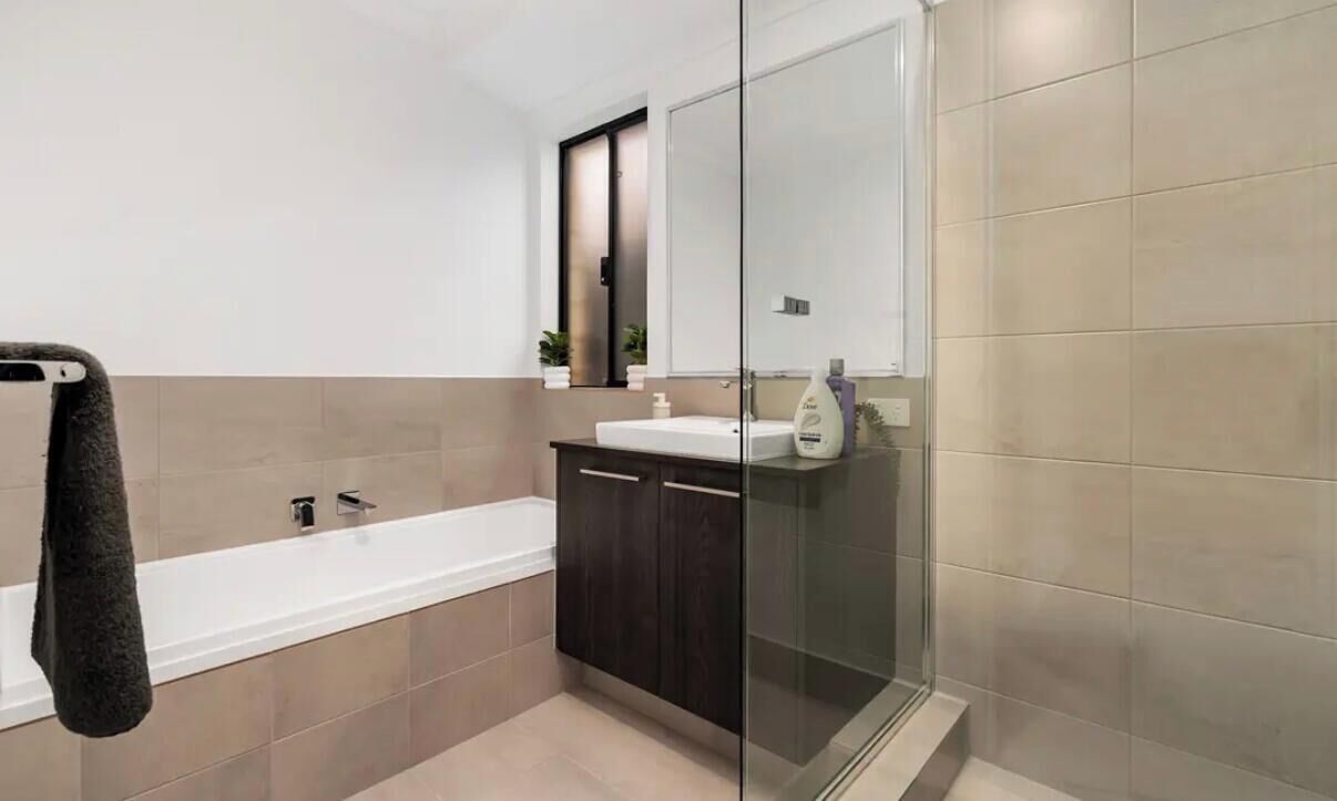 A modern bathroom with a glass shower enclosure, a bathtub, and dark wooden cabinets.