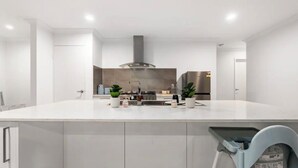 Een moderne keuken met een centraal kookeiland, roestvrijstalen apparatuur en een grijze afzuigkap.