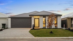 Een modern huis met twee verdiepingen, een garage, een verzorgd gazon en een kleine boom in de voortuin.