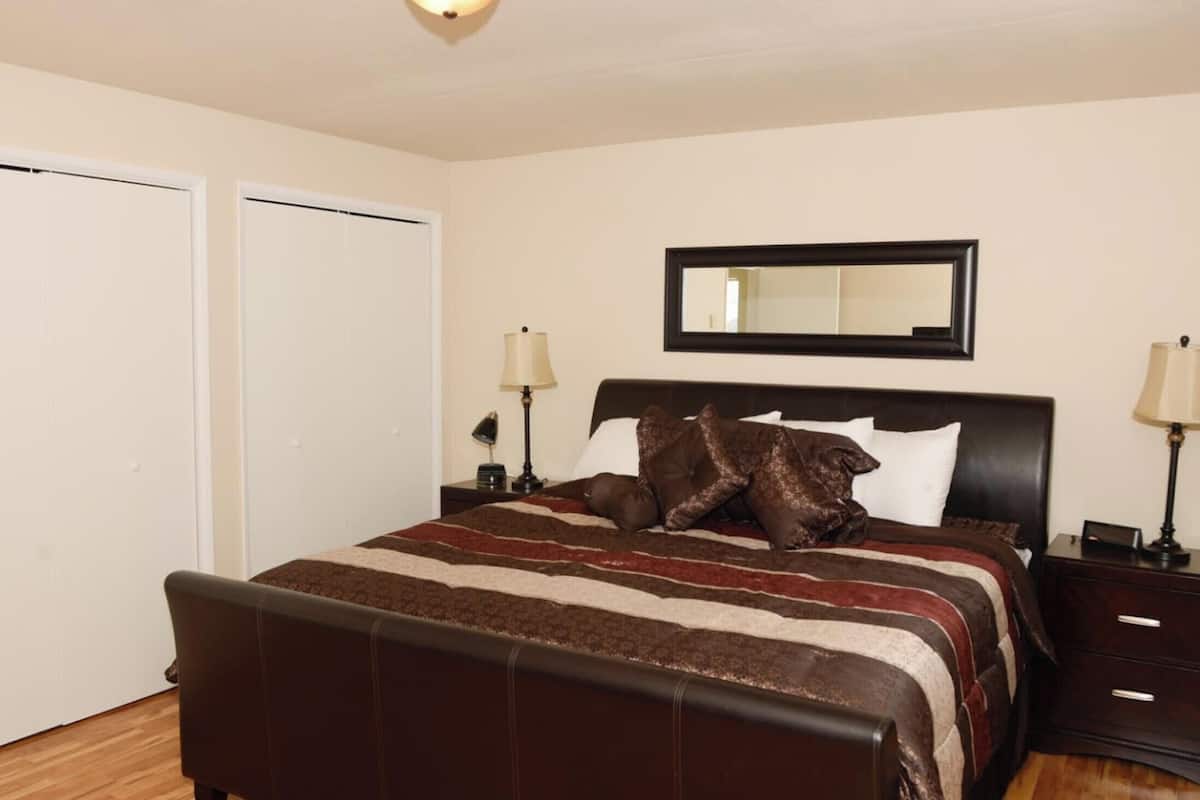 A bedroom with a bed, two bedside tables, a nightstand, a mirror, and a wardrobe.