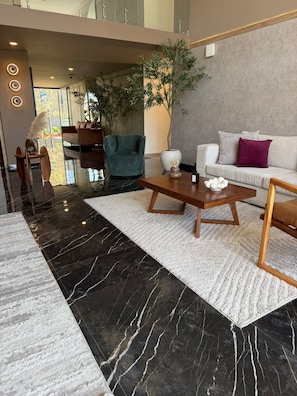 Ein modernes Wohnzimmer mit Marmorboden, einem Holztisch, einem grünen Sessel, einem weißen Sofa und einer großen Pflanze.