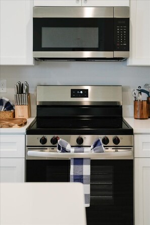 Uma cozinha com micro-ondas, fogão, forno e um conjunto de facas na bancada.
