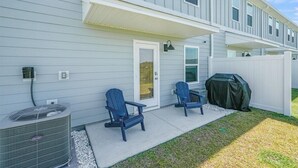 Ein Wohnhaus mit überdachter Veranda, zwei Adirondack-Stühlen, einem Grill und einer Klimaanlage.