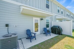 Ein Wohnhaus mit überdachter Veranda, zwei Adirondack-Stühlen, einem Grill und einer Klimaanlage.