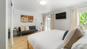 A modern bedroom with a large bed, a sofa, a TV mounted on the wall, and a window with curtains.