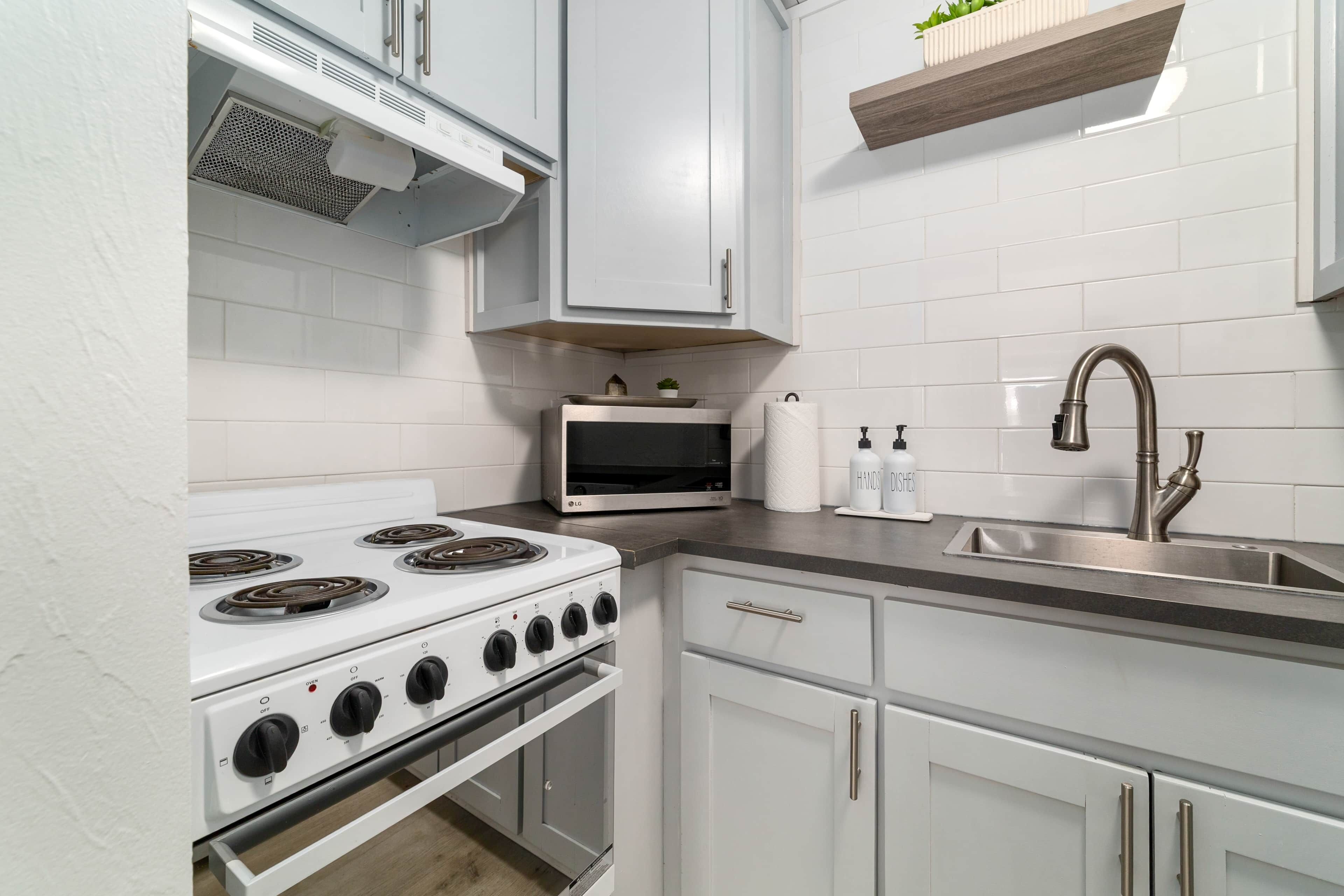 Een keuken met witte kastjes, een kookplaat, een magnetron en een spoelbak.