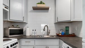 Cocina compacta con armarios blancos, horno empotrado, microondas, lavamanos y lavadora.