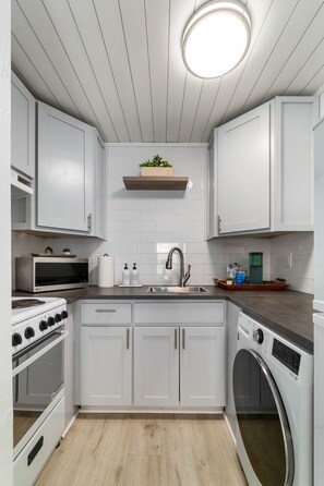 A compact kitchen with white cabinets, a built-in oven, a microwave, a sink, and a washing machine. - Ivory & Ocean •walk to Lido beach •private patio (Sarasota)