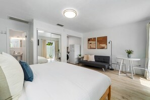 Een moderne hotelkamer met een groot bed, een sofa, een klein tafeltje en uitzicht op de keuken en badkamer.