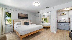 Un dormitorio moderno con una cama de madera, una mesita de noche pequeña, un espejo y vistas al exterior.