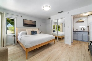A modern bedroom with a wooden bed, a small bedside table, a mirror, and a view of the outside. - Ivory & Ocean •walk to Lido beach •private patio (Sarasota)