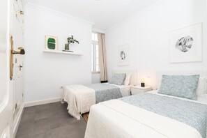 Un dormitorio con dos camas, una mesita de noche, una ventana con cortinas y decoración en la pared.