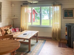 A cozy room with a wooden table, a sofa with a teddy bear, a window with curtains, a radiator, and a fireplace. - 8 Person Holiday Home in Brandtorp (Brandstorp)