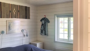 Et soveværelse med en seng, et lille natbord, en vægmonteret lampe, et indrammet billede, et vindue med udsigt og en ophængt bøjle.