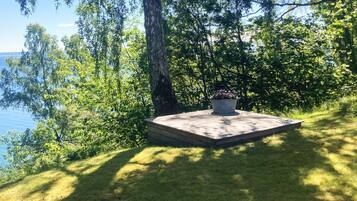 A wooden deck with a planter, surrounded by trees and grass, overlooking a body of water.