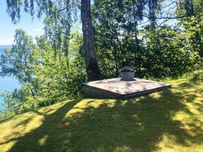 A wooden deck with a planter, surrounded by trees and grass, overlooking a body of water. - 8 Person Holiday Home in Brandtorp (Brandstorp)