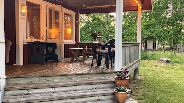 En træterrasse med en overdækket veranda, et spisebord med stole og krukkeplanter.