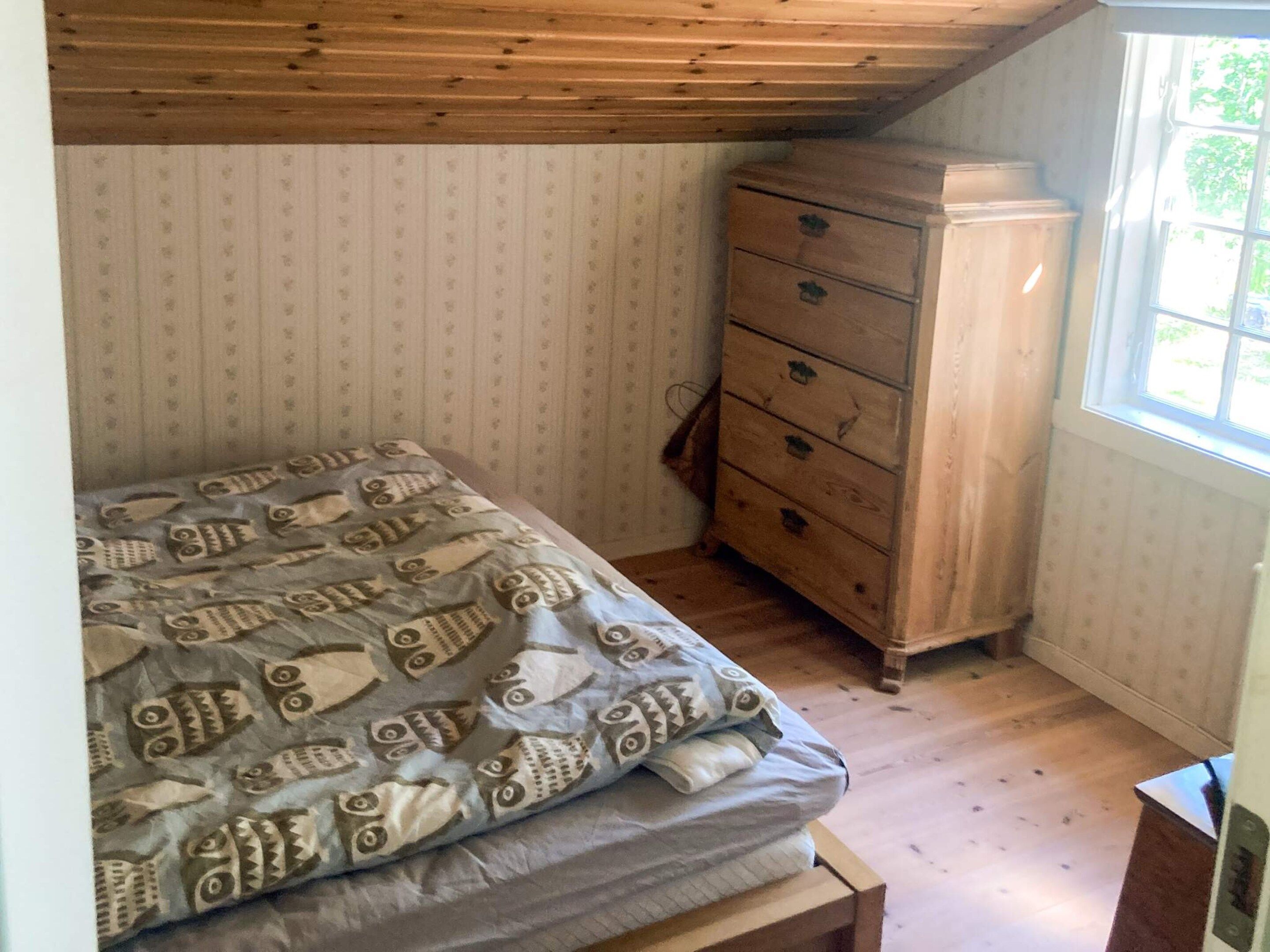 Une petite chambre à coucher avec un lit, une commode en bois et une fenêtre.