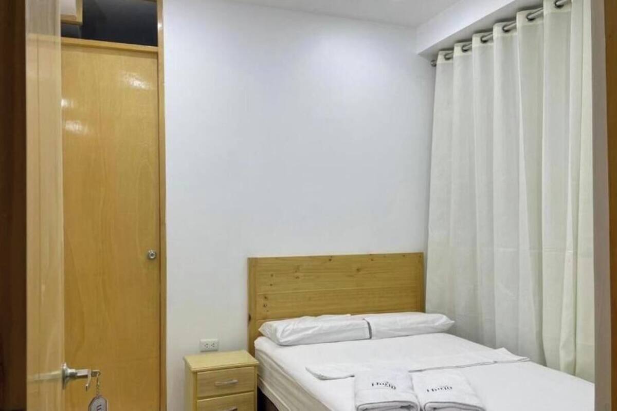 Un dormitorio con cabecera de madera, una cama individual con ropa blanca, una mesita de noche y una puerta con un llavero.