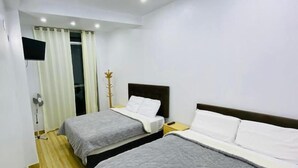 Habitación de hotel con dos camas, un televisor de pantalla plana montado en la pared, piso de madera y una ventana con cortinas.