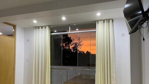 Una habitación con un gran ventanal corredera, piso de madera y televisor en el techo.
