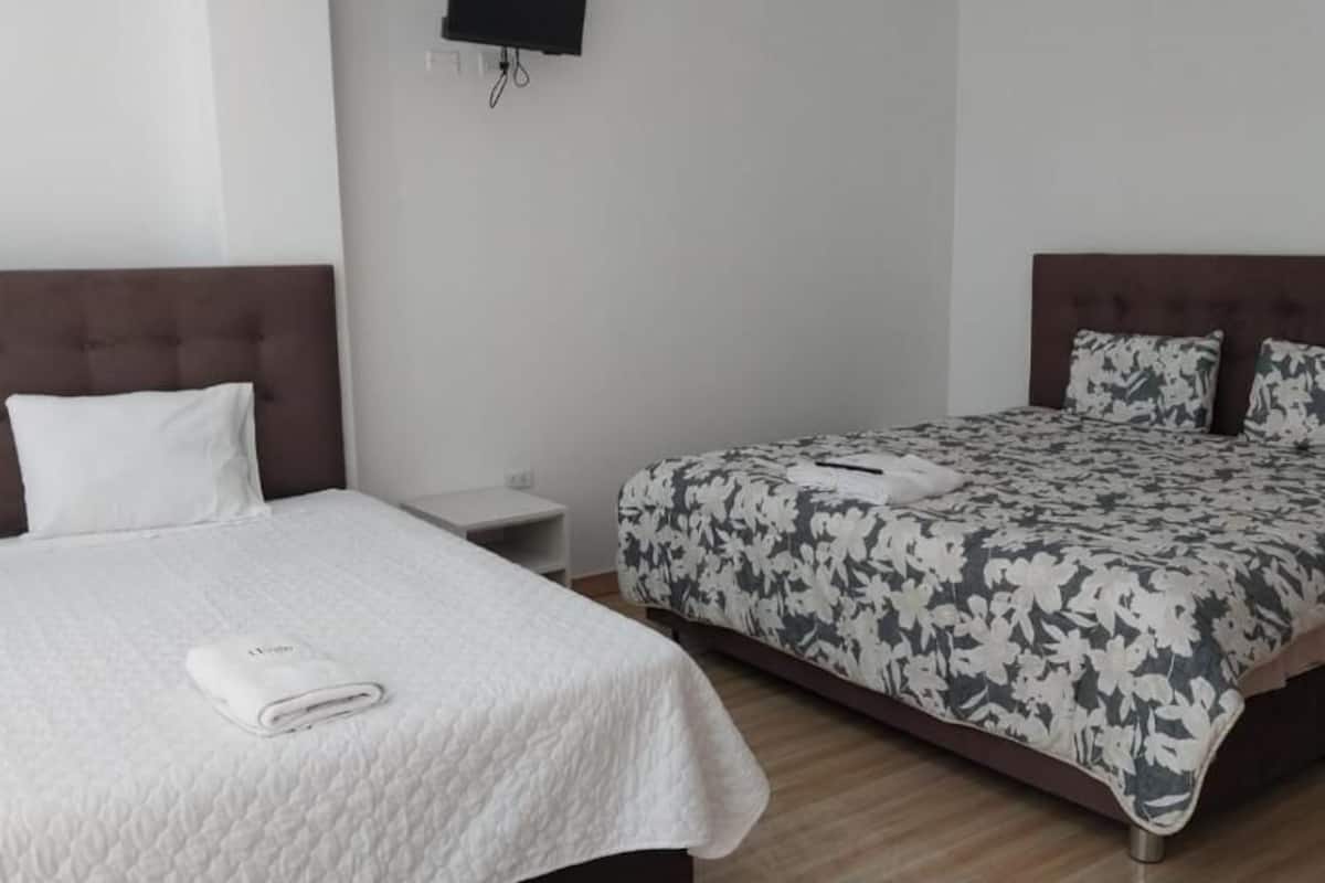 Un dormitorio con cama, mesita de noche y televisor en la pared.