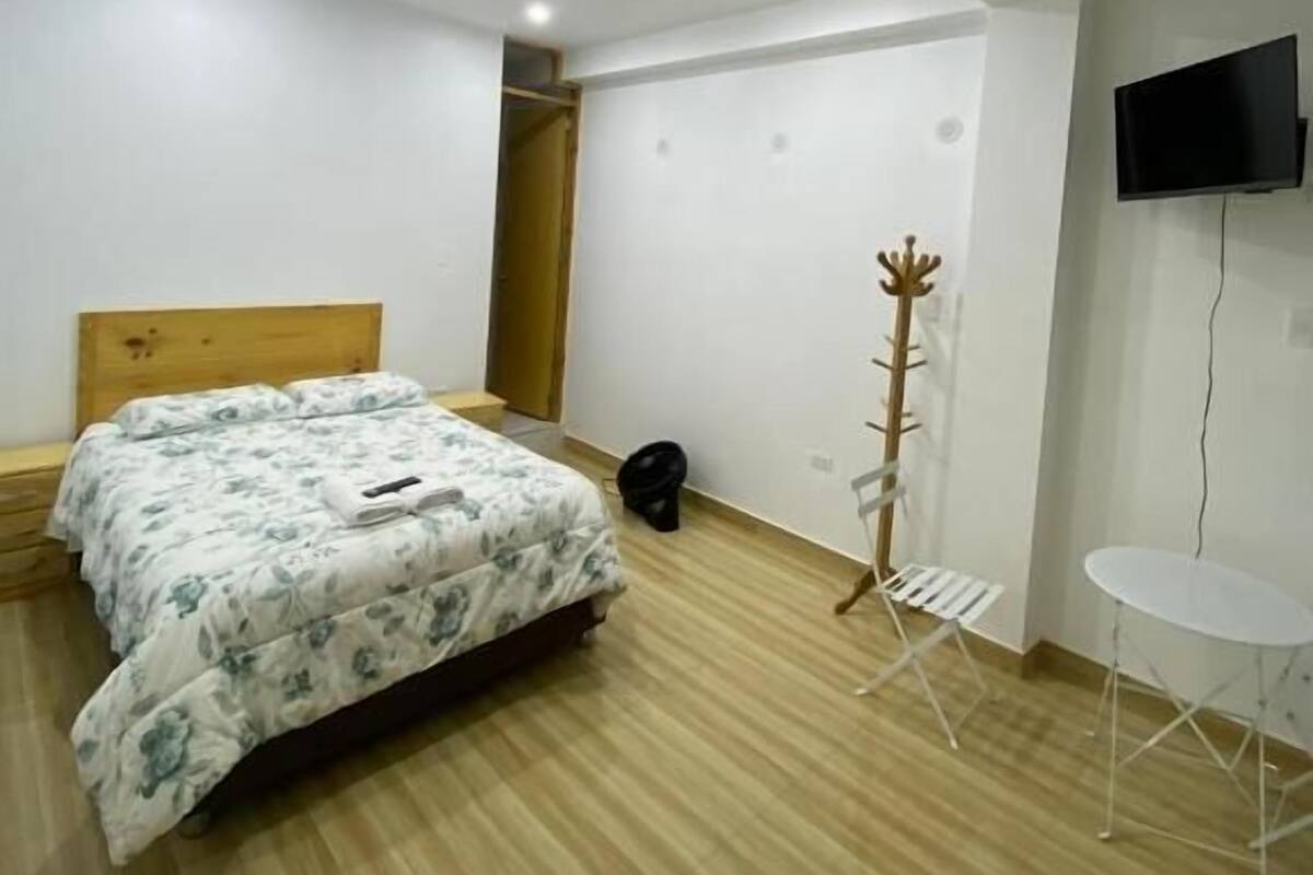 Un dormitorio con cama, una silla, televisor y perchero.