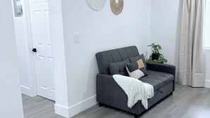 Un salon moderne avec un canapé gris, une porte blanche et une plante posée sur une table d’appoint.