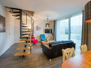Ein modernes Wohnzimmer mit Wendeltreppe, Flachbildfernseher, Sofa und Esstisch.