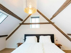 Ein Schlafzimmer mit schrägem Dach, einem Bett, einem Nachttisch, einer Lampe und einem Fenster.