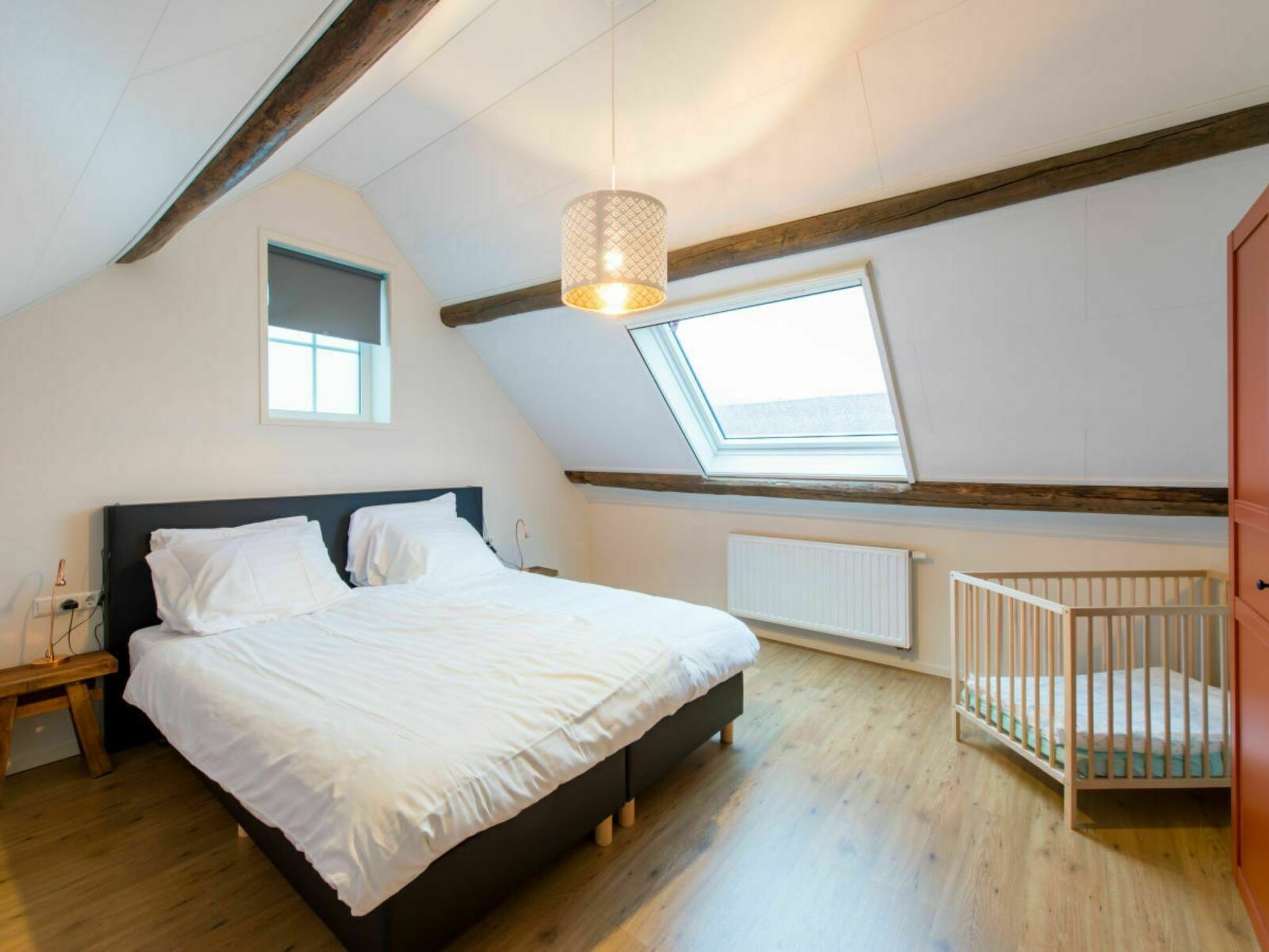 Un dormitorio con una cama, una cuna, un tragaluz, una ventana y techo de madera.