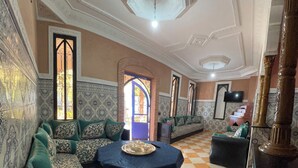 A room with a checkered floor, patterned walls, a sofa set, a dining table with a tray, and a television.