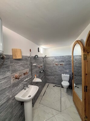 Une salle de bain équipée d’un lavabo, de toilettes, d’une douche et d’une porte en bois.