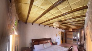 A bedroom with a wooden bed, a nightstand, a window with curtains, and a ceiling with wooden beams.