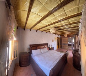 Une chambre à coucher avec un lit en bois, une table de chevet, une fenêtre avec des rideaux et un plafond avec des poutres en bois.