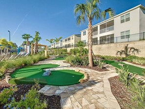 Ein Golfplatz mit Putting-Green, Palmen und einem Gebäude mit Balkonen.