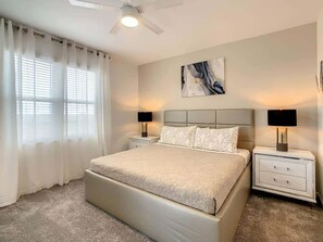 Ein Schlafzimmer mit einem Bett, zwei Nachttischen, einem Deckenventilator und einem großen Fenster mit Vorhängen.