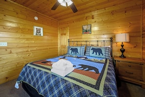 Ein Holzblockraum mit Bett, Nachttisch, Lampe und Deckenventilator.